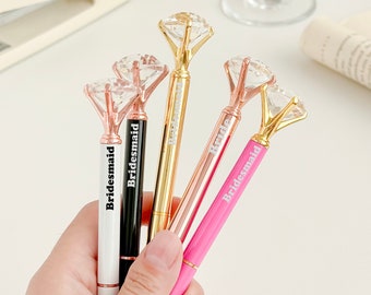 May include: Five diamond-shaped pens with gold tops and different colored barrels. The pens are labeled "Bride" and "Bridesmaid".