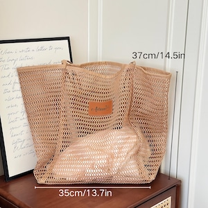 May include: A beige mesh tote bag, 14.5 inches tall and 13.7 inches wide, with a leather patch that reads "Aileen". The bag is filled with a light-colored item. The text "When I write a letter to you..." is visible in the background.
