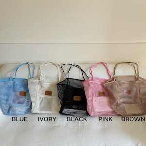 May include: Five mesh tote bags in blue, ivory, black, pink, and brown. Each bag has a rectangular leather patch and matching handles. The colors are labeled below each bag. The bags are sitting on a white surface.