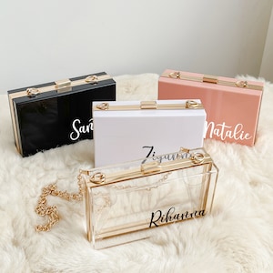 Può includere: Tre pochette rigide in acrilico trasparente con dettagli dorati e catene. Le pochette sono personalizzate con i nomi "San", "Ziggy" e "Rihanna".