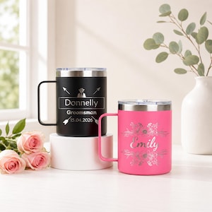 May include: Two stainless steel travel mugs with handles. One is black with the name "Donnelly" and "Groomsman" and the date "15.04.2026". The other is pink with the name "Emily" and floral design.