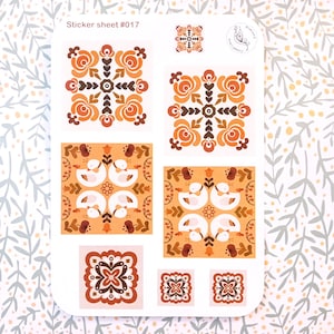 Könnte beinhalten: Ein Stickerbogen mit verschiedenen Designs in Orange, Braun und Weiß. Die Designs umfassen florale Muster und Schwanenmotive. Der Text "Sticker sheet #017" ist oben sichtbar. Ein kleines Logo ist ebenfalls vorhanden.