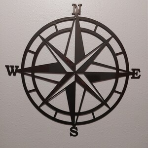 May include: Black metal compass with a traditional design. The compass features the cardinal directions N, S, E, and W.