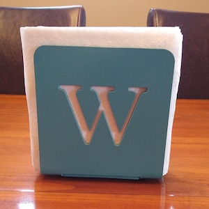 May include: Teal metal napkin holder with a white paper napkin and the letter "W" cut out of the front.