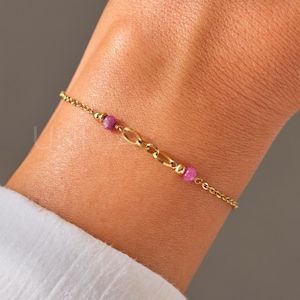 Puede incluir: Un brazalete de cadena dorada con pequeñas cuentas de piedras preciosas rosas.