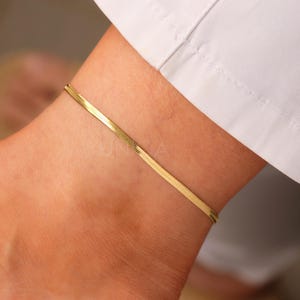 Op de afbeelding: Een gouden enkelketting met een delicaat, plat, slangkettingontwerp.