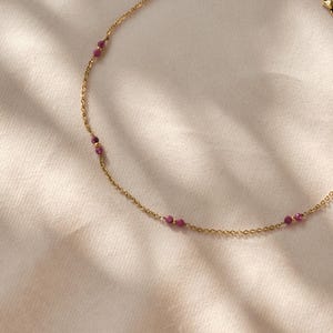 Peut inclure: Un collier délicat en chaîne dorée avec de petites pierres précieuses rose foncé espacées uniformément.