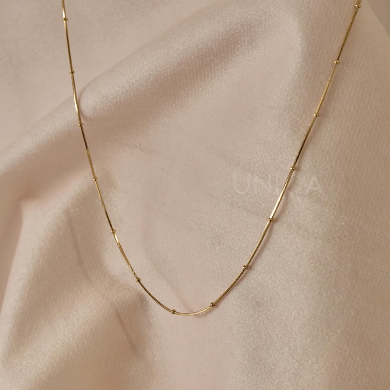 May include: A gold chain necklace with small round beads. The chain is delicate and has a simple design.