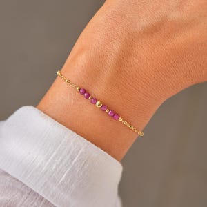 May include: A delicate gold chain bracelet with small pink beads and gold accents.