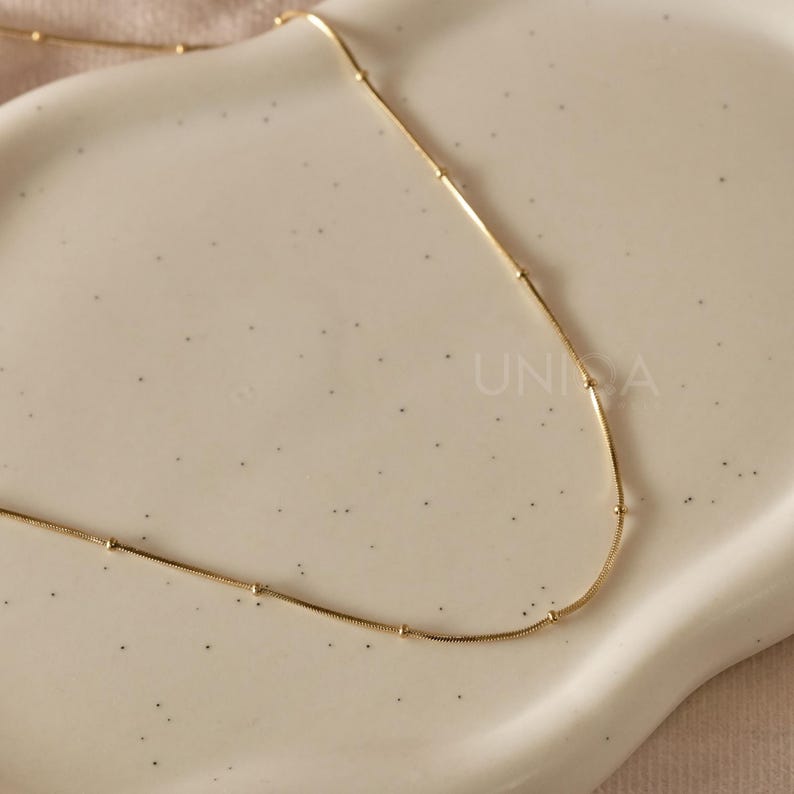 May include: A gold chain necklace with small round beads spaced evenly along the chain.