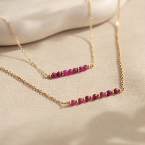 May include: Two gold necklaces with a row of pink gemstone beads. The necklaces are layered on top of each other.