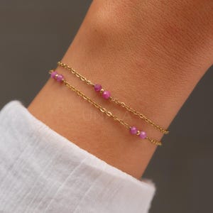 Op de afbeelding: Een delicate gouden kettingarmband met kleine roze kralen. De armband is gelaagd, met twee kettingen en kralen.