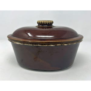 Può includere: Una pirofila in ceramica marrone scuro con coperchio abbinato. Il contenitore presenta una finitura liscia e lucida sul corpo e sul coperchio, con una fascia decorativa testurizzata e maculata color crema e marrone sul bordo.