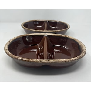 Puede incluir: Dos fuentes de cerámica marrón divididas. Cada plato ovalado tiene un divisor central, creando dos compartimentos. Los bordes tienen un acabado texturizado marrón claro, que contrasta con el interior marrón oscuro brillante. Ideal para servir aperitivos.