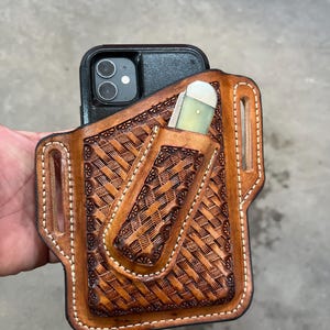 May include: A brown leather phone and pocket knife holster with a woven pattern. The holster has a stitched edge and a belt loop.
