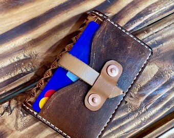 May include: A brown leather card holder with a tan leather strap and a blue credit card inside. The card holder has a stitched edge and a distressed look.