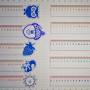 Peut inclure: Un ensemble de dix marque-pages en forme de règle bleus et turquoise avec diverses illustrations sur le thème des animaux et de la nature. Les marque-pages sont imprimés sur un fond blanc et comportent une règle avec des chiffres de 0 à 15.