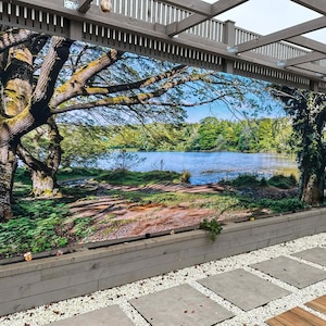 May include: A large outdoor mural showing a tranquil landscape with a lake, trees, and a blue sky. The mural is mounted on a wooden structure, with a stone walkway and gravel in the foreground. The scene evokes a sense of peace and nature.