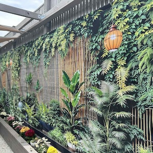 Könnte beinhalten: Eine lebendige Außenszene mit einem üppigen vertikalen Garten. Das Design integriert einen Bambushintergrund, der mit verschiedenen grünen Pflanzen und hängenden Laternen geschmückt ist. Ein Blumenbeet mit bunten Blüten ergänzt die natürliche Ästhetik.