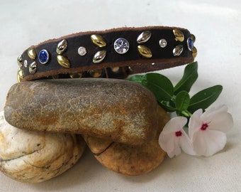 May include: A brown leather dog collar with gold and silver studs and blue and clear rhinestones.