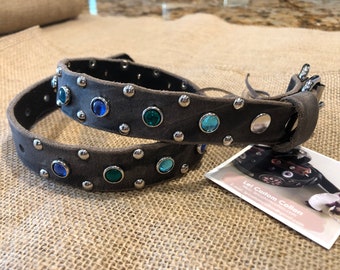 May include: A gray leather dog collar with silver studs and colorful rhinestones. The collar is shown folded in half, with the buckle visible on the right side. The text "Lei Custom Collars" is visible on a business card in the lower right corner.