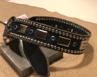 May include: A black leather dog collar with silver studs and blue rhinestones. The collar has a silver nameplate with the text "JAXSON 516-515" engraved on it.