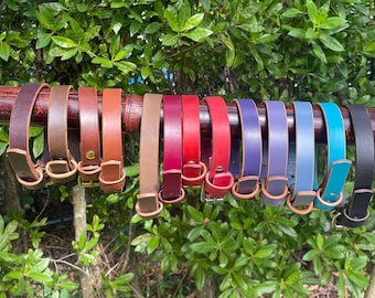 May include: A collection of 14 leather collars in various colors, including brown, tan, red, purple, blue, and black. The collars are displayed on a wooden rod.