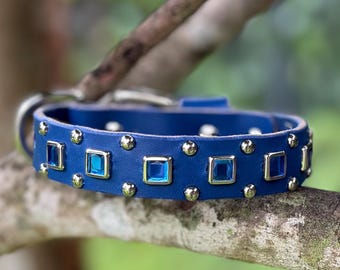 May include: A blue leather collar featuring a series of square, bright blue faceted gemstones set in silver-toned metal frames, alternating with small, round, silver-toned metal studs along the entire length of the band.