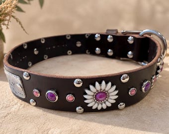 May include: A dark brown leather collar featuring a silver-toned metal buckle and D-ring. The collar is decorated with a white and purple daisy-shaped embellishment, smaller purple and pink circular stones, and silver-toned metal rivets.