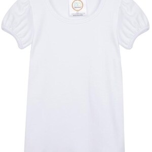 May include: A white short-sleeved top with a round neckline and puffed sleeves. The garment has a tag near the neckline with text. The top is made of a soft, lightweight fabric.