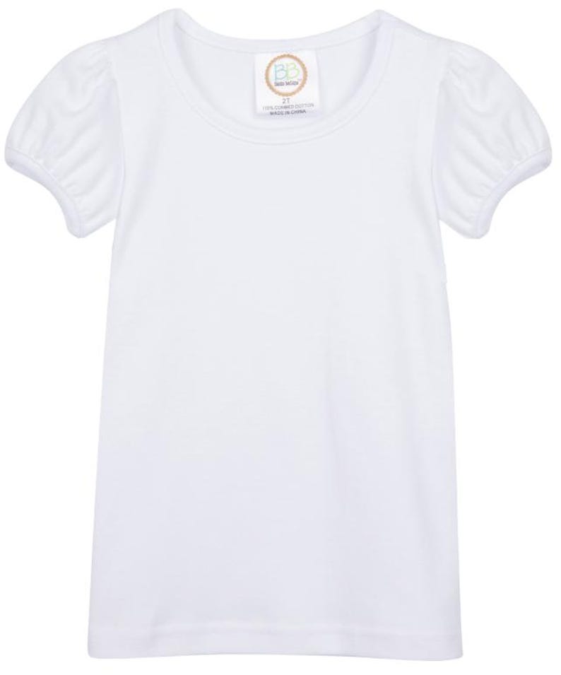 May include: A white short-sleeved top with a round neckline and puffed sleeves. The garment has a tag near the neckline with text. The top is made of a soft, lightweight fabric.