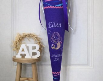 May include: A dark purple fabric cone with a mermaid illustration, the name Ellen, and the text Schulkind 2021. The cone features a wavy pink pattern, a dark purple ribbon tie at the top, and light blue and pink horizontal wavy lines.