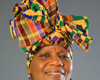 May include: A woman wearing a white shirt with a colorful patterned head wrap. The head wrap is tied in a knot at the top of her head and has a bow on the side. She is wearing large hoop earrings.