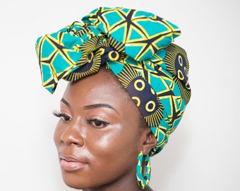 May include: A woman wearing a green, yellow, and black patterned head wrap with a large bow. She is wearing large hoop earrings that match the colors of the head wrap.