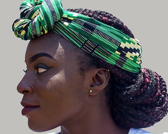 May include: A woman with dark brown hair styled in braids wears a green, yellow, and black patterned head wrap. The wrap is tied in a knot on top of her head. She is wearing a white t-shirt.