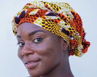 May include: A woman wearing a colorful head wrap with a yellow, orange, brown, and white pattern. The wrap is tied in a turban style.