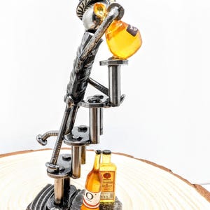 Può includere: Scultura in metallo realizzata a mano di un barista che versa da bere. La scultura presenta una figura con un cappello a cilindro, con una bottiglia e un bicchiere. La scultura è posta su una base di legno, con due bottiglie in miniatura.