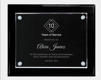 May include: A black plaque with a silver frame and a clear acrylic insert. The plaque has a silver diamond with the number 10 inside. The text reads "10 Years of Service", "Presented To", "Alicia Juarez", "In recognition of your outstanding sales efforts and achievements", and "August 2022".