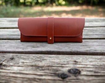 May include: A brown leather pencil case with a gold snap closure.