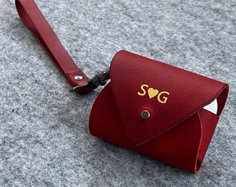May include: A crimson leather pouch with a wrist strap and a press stud closure. The pouch features gold lettering reading "S ♥ G". The case is designed for small items and has a metal clasp.