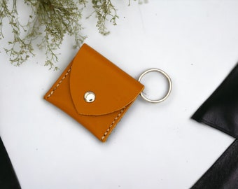 May include: A small, mustard yellow leather key chain with a single pocket and a silver key ring.