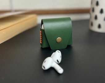May include: A green leather case with orange stitching and a gold button closure. The case is designed to hold wireless earbuds.
