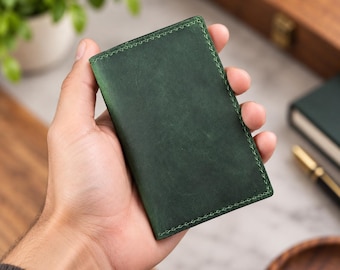 May include: A rectangular forest green leather card holder or wallet featuring a smooth matte finish and visible tonal stitching along all four edges. The item is compact and displays a consistent deep green color across its entire surface.