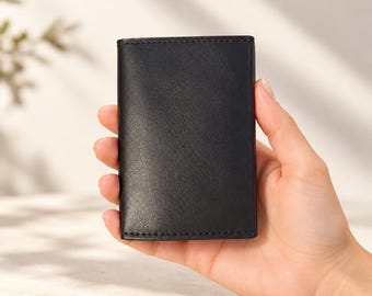 May include: A rectangular black leather card holder with a smooth, matte finish and visible stitching along the edges. The item is compact, featuring a clean, minimalist design with a vertical orientation and a simple, unadorned front surface.