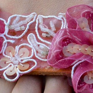 K&ouml;nnte beinhalten: Rosa Stoff-Sandalen mit wei&szlig;er Spitze und perlenartigen Verzierungen.