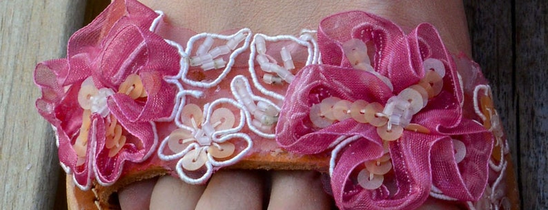 K&ouml;nnte beinhalten: Rosa Stoff-Sandalen mit wei&szlig;er Spitze und perlenartigen Verzierungen.