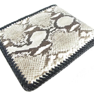 May include: A bi-fold wallet featuring a textured snakeskin pattern in shades of cream, beige, and dark brown. The edges of the wallet are finished with a thick, black braided leather trim that runs along the entire perimeter of the rectangular object.