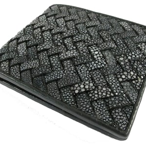 Puede incluir: Una cartera plegable de color negro con un patrón exterior trenzado. La superficie está compuesta por un material texturizado similar a cuentas con un acabado oscuro y brillante. Los bordes son lisos y negros, creando una forma rectangular.
