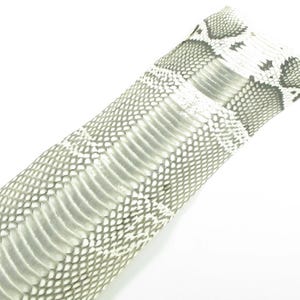 May include: A rectangular piece of snakeskin leather featuring a repeating diamond pattern in shades of white, light gray, and dark gray. The texture displays the natural, overlapping scale structure characteristic of reptile skin with a smooth finish.