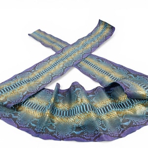 May include: A long, flexible strip of snakeskin leather featuring a vibrant gradient pattern. The texture displays a detailed scale motif in shades of deep purple, metallic gold, and bright turquoise, arranged in a repeating, symmetrical diamond-like geometric design.
